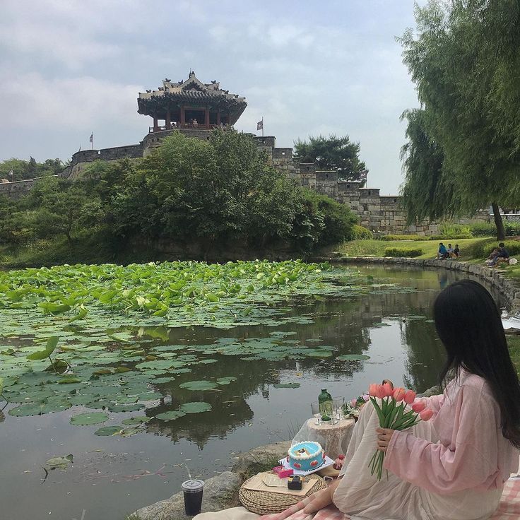 a woman sitting on the edge of a pond with water lillies in front of her