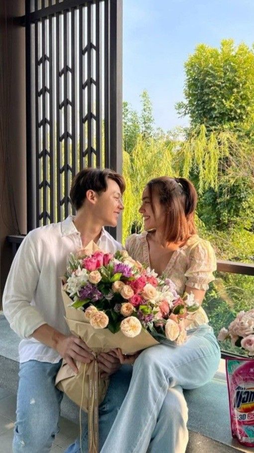 a man and woman sitting on the steps with flowers in front of them, one holding a bouquet