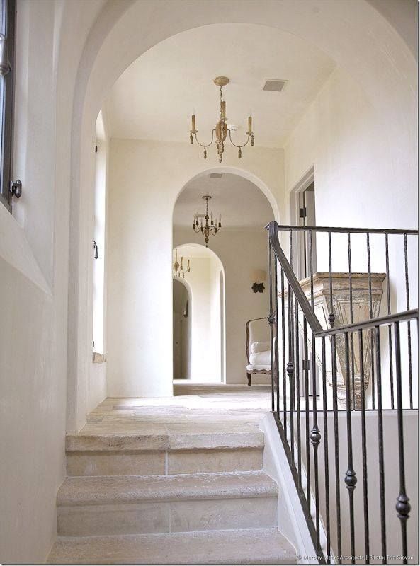 an arched hallway with stairs and chandelier