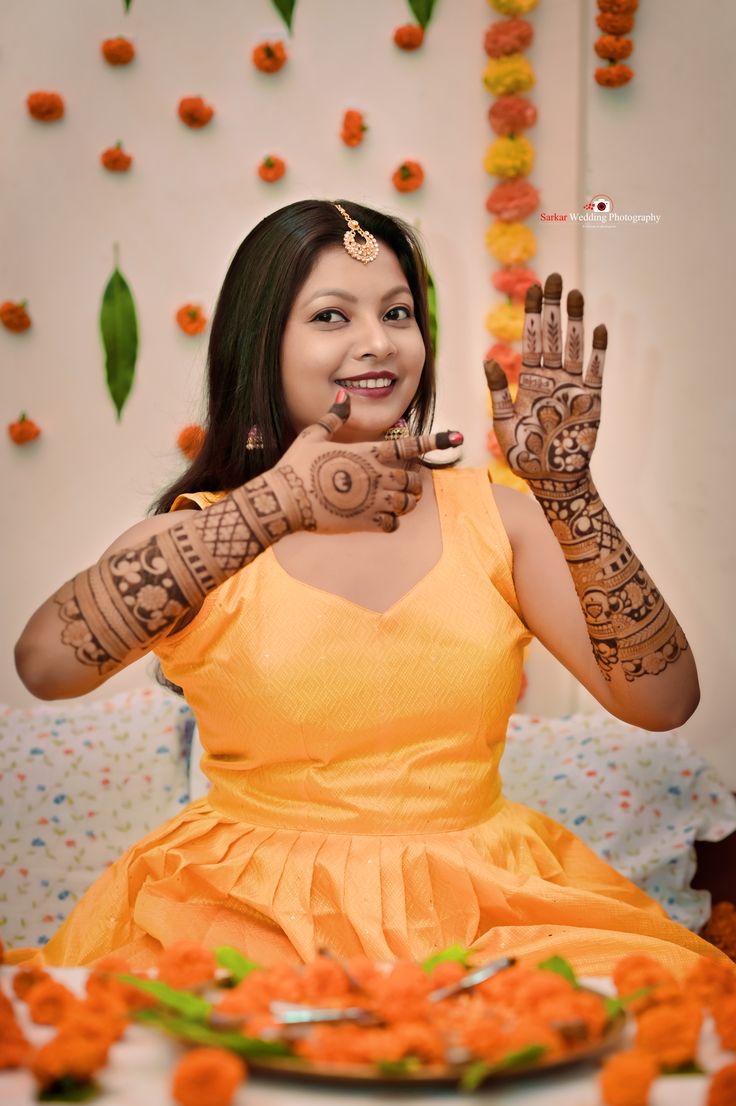 a woman with henna on her hands sitting in front of an arrangement of flowers