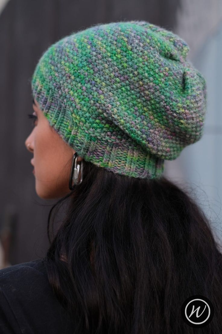 a woman wearing a green and grey knitted hat with large hoop earrings on her ear