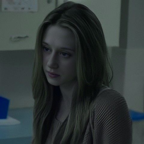 a young woman sitting in front of a computer monitor looking at the camera while wearing a sweater