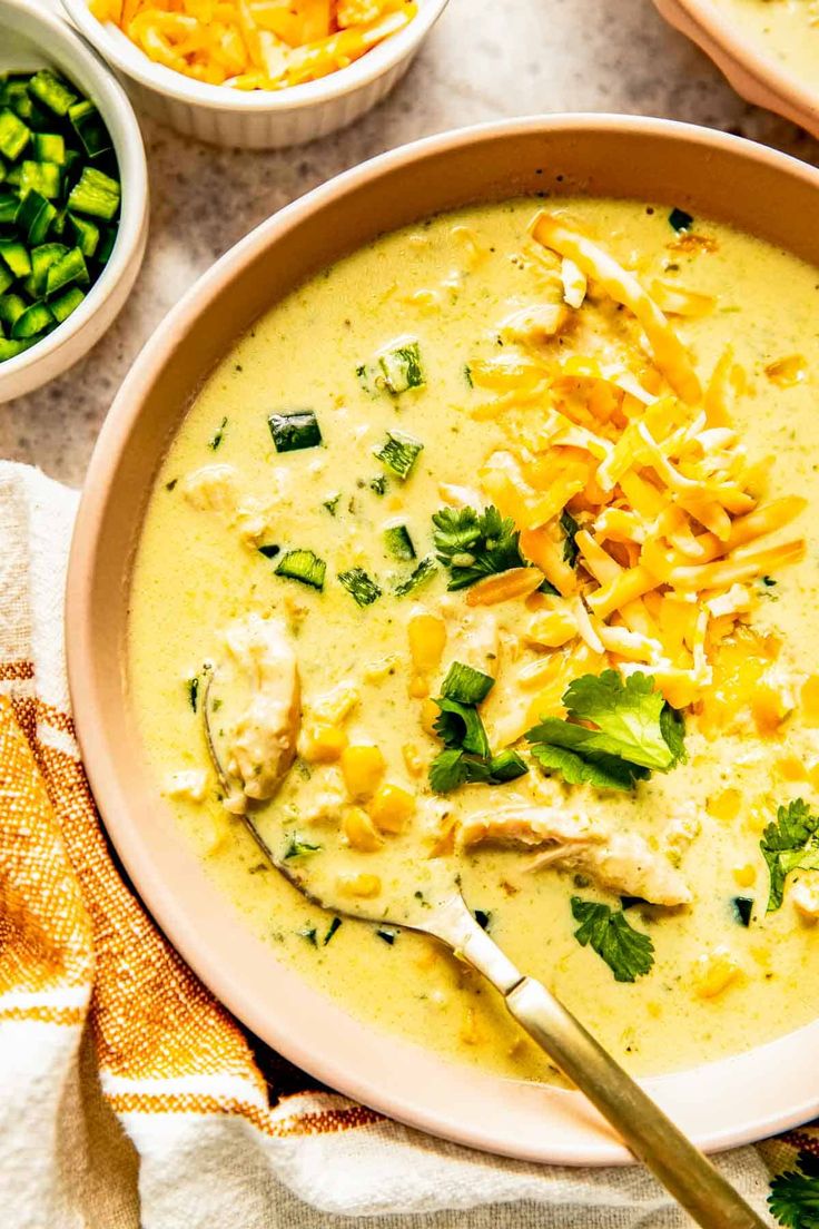 a bowl filled with soup next to bowls of vegetables and cheese on a table top