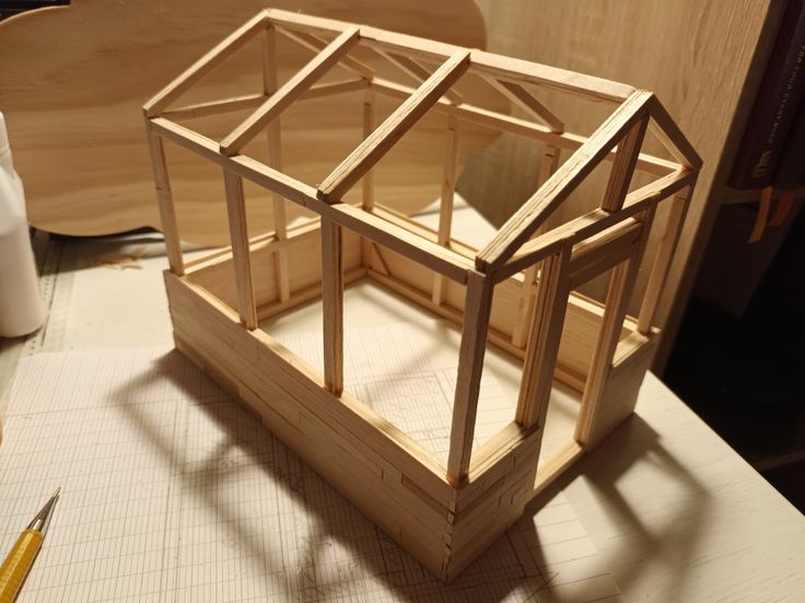 a wooden model of a house sitting on top of a table next to a ruler