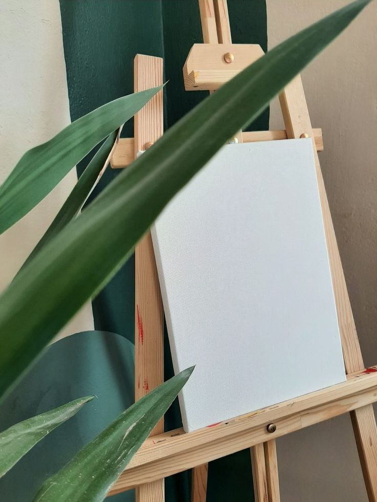 an easel with a white canvas on it next to a green leafy plant