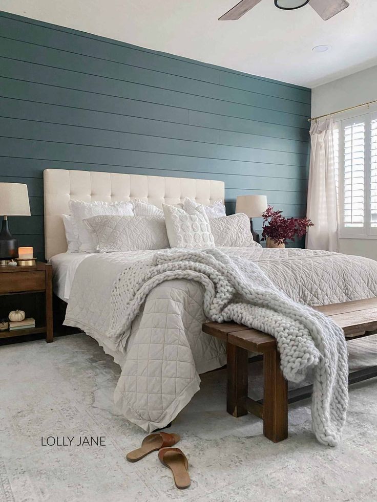 a bedroom with blue walls, white bedding and a bench in front of the bed