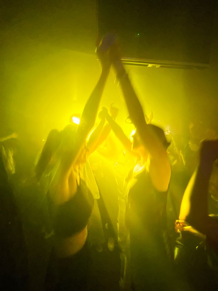 several people are dancing in the dark with their arms up and lights on behind them