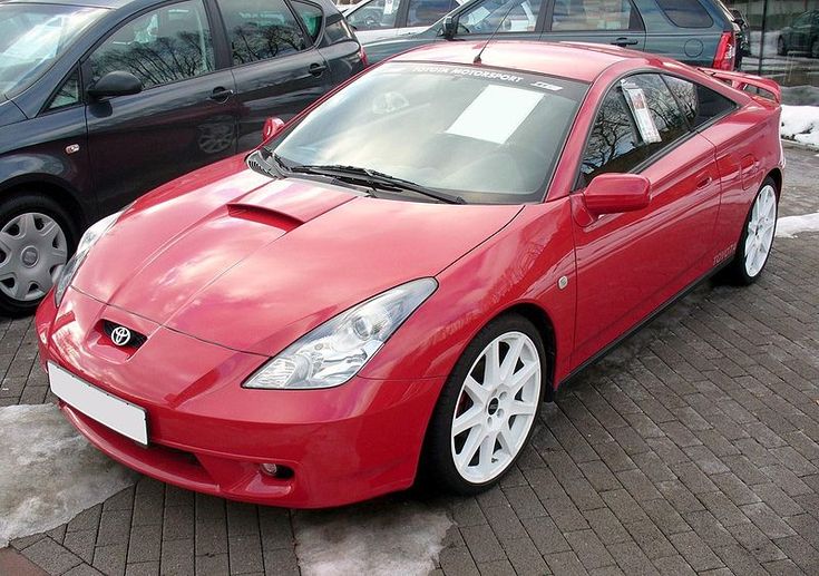 a red sports car parked next to other cars in a parking lot with snow on the ground