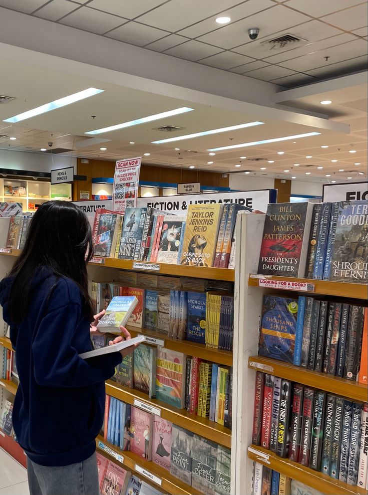 a woman standing in front of a bookshelf holding a book and looking at it