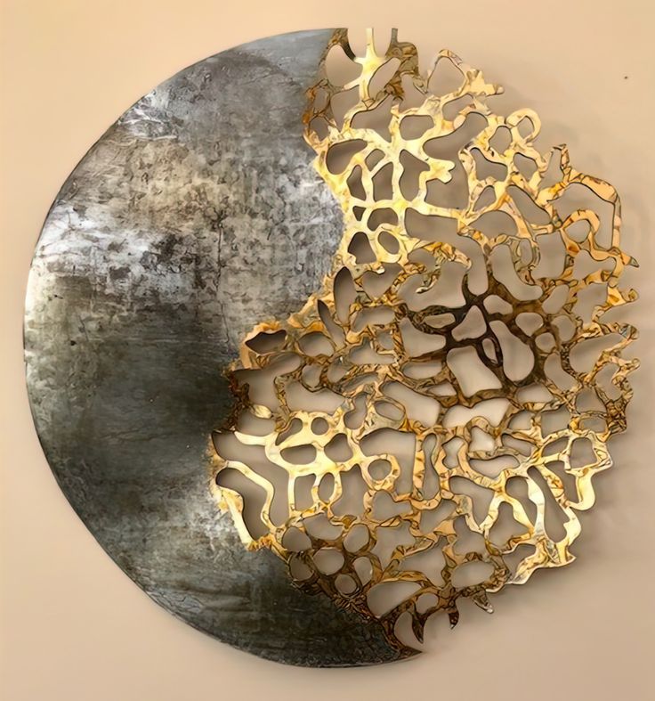 a circular metal plate with gold and silver designs on the top, in front of a white wall