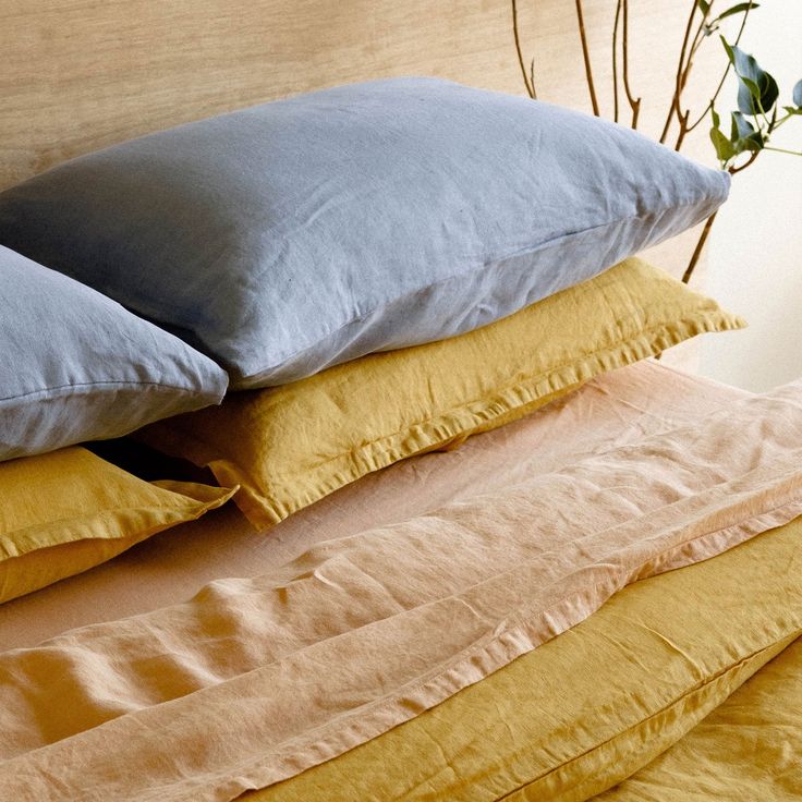 a stack of pillows sitting on top of a bed next to a vase with flowers