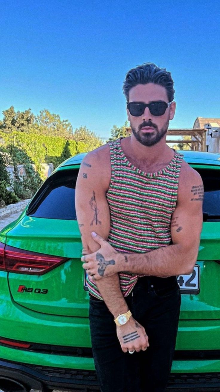 a man standing in front of a green car with tattoos on his arm and chest