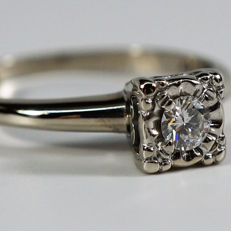 a white gold engagement ring with an old - fashioned diamond in the center, on a plain surface