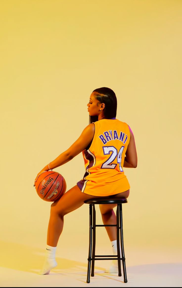 a woman in an orange basketball uniform sitting on a stool with her foot up and holding a basketball