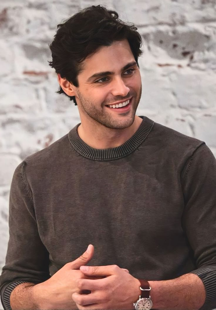 a smiling man sitting at a table with his hands crossed and looking to the side