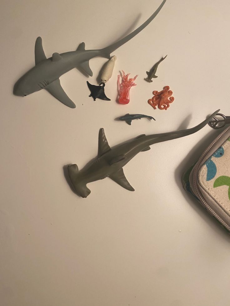 several toy sharks and sea creatures are on the table next to a zippered pouch