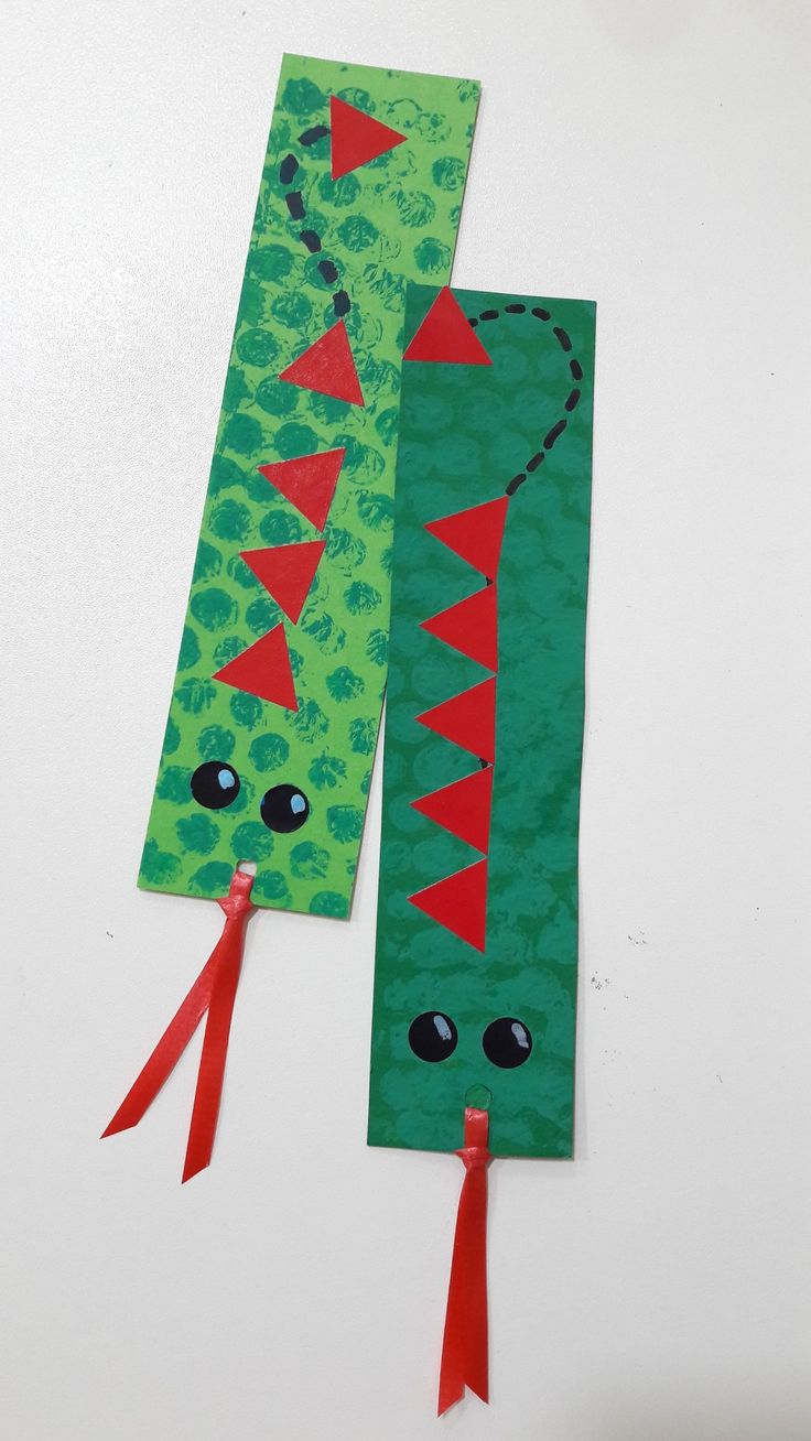 two bookmarks made to look like dinosaurs with red ribbon ties on the ends and eyes