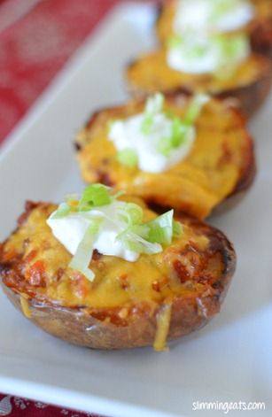 three baked potatoes with cheese and green onions on them sitting on a white platter