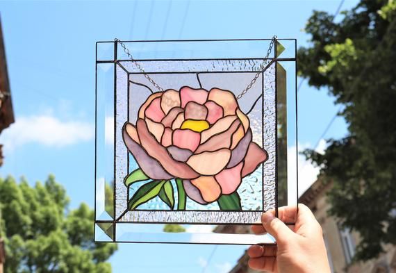 a hand holding up a stained glass window with a flower on it's side