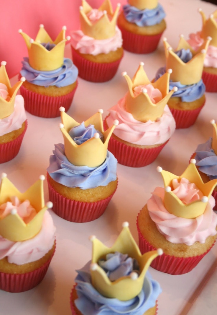 cupcakes with frosting and crowns on them are sitting on a tray, ready to be eaten