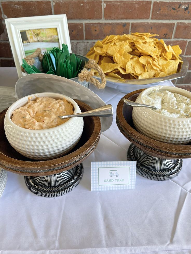 two bowls filled with dips and chips on top of a white tablecloth covered table