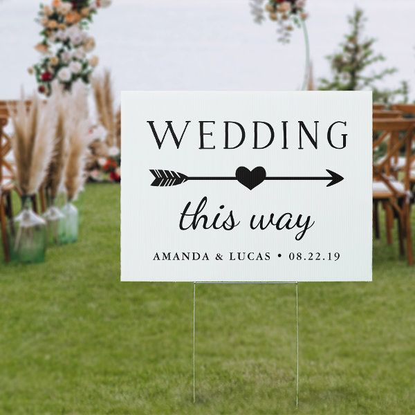 a sign that says wedding this way with an arrow and heart on it in the grass