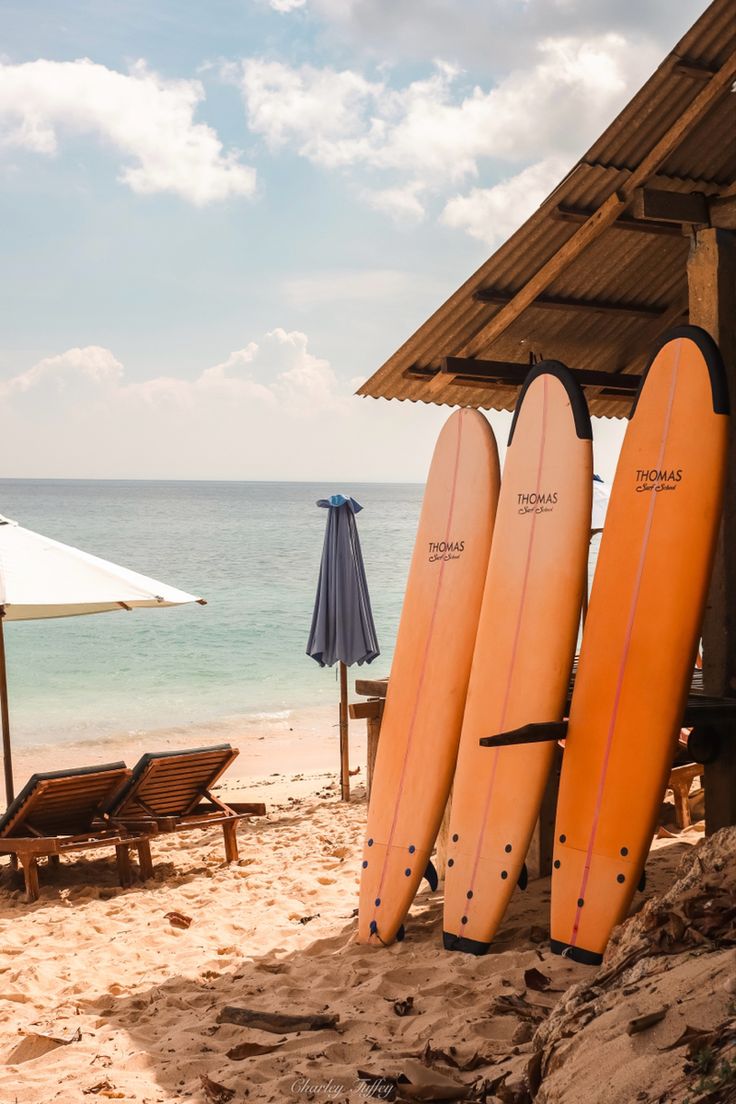 three surfboards are leaning against the wall on the beach near chairs and umbrellas