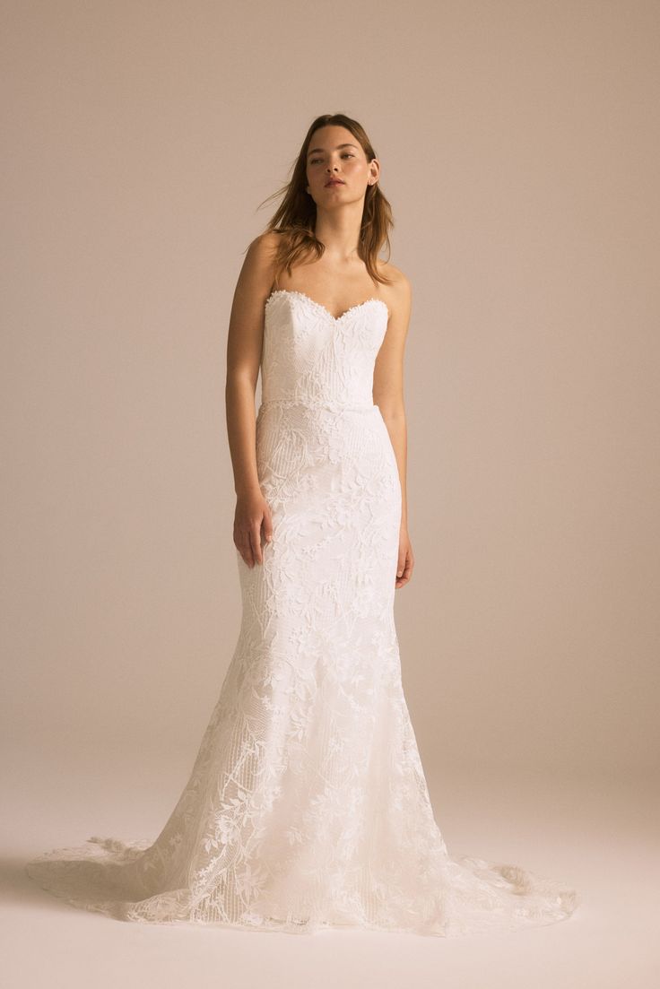 a woman in a white wedding dress standing against a beige background with her hands on her hips