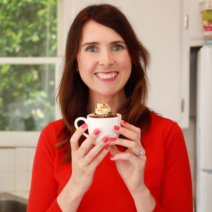 a woman in a red shirt is holding a white cup with food on it and smiling at the camera