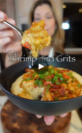 a woman eating food from a black bowl on top of a wooden table with the words shrimp and grits in front of her