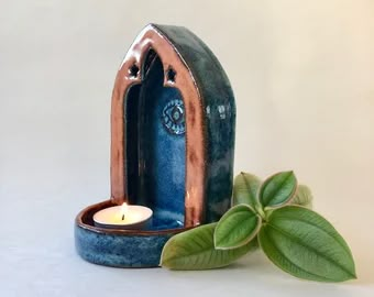 a small blue candle holder with a green leaf next to it on a white surface