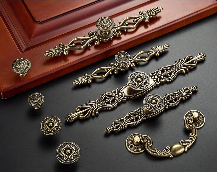 antique brass drawer pulls and knobs on a black surface next to a wooden frame