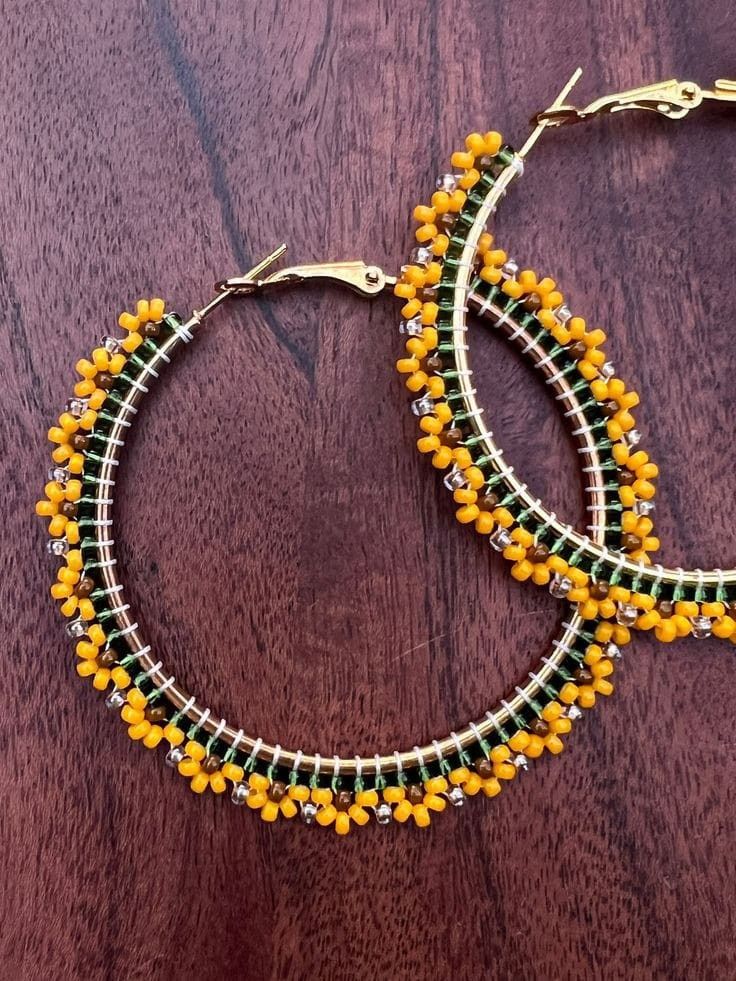 two yellow and green beaded hoop earrings sitting on top of a wooden table next to each other