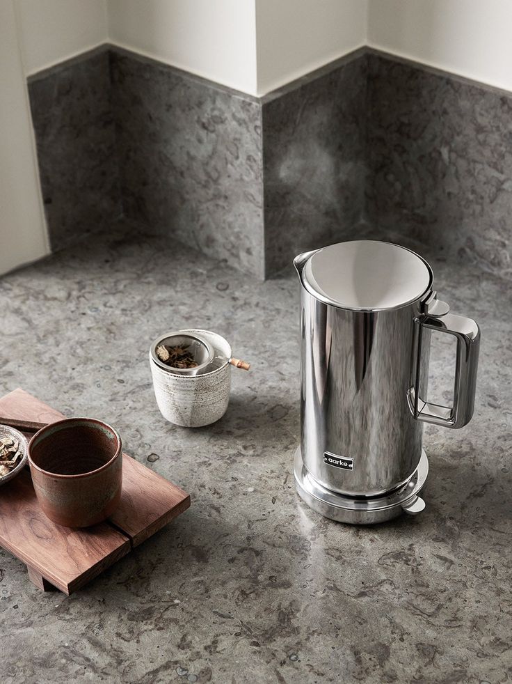 a stainless steel coffee pot sitting on top of a counter next to a wooden tray