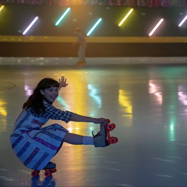 a young woman riding a skateboard on top of a ice rink in front of neon lights