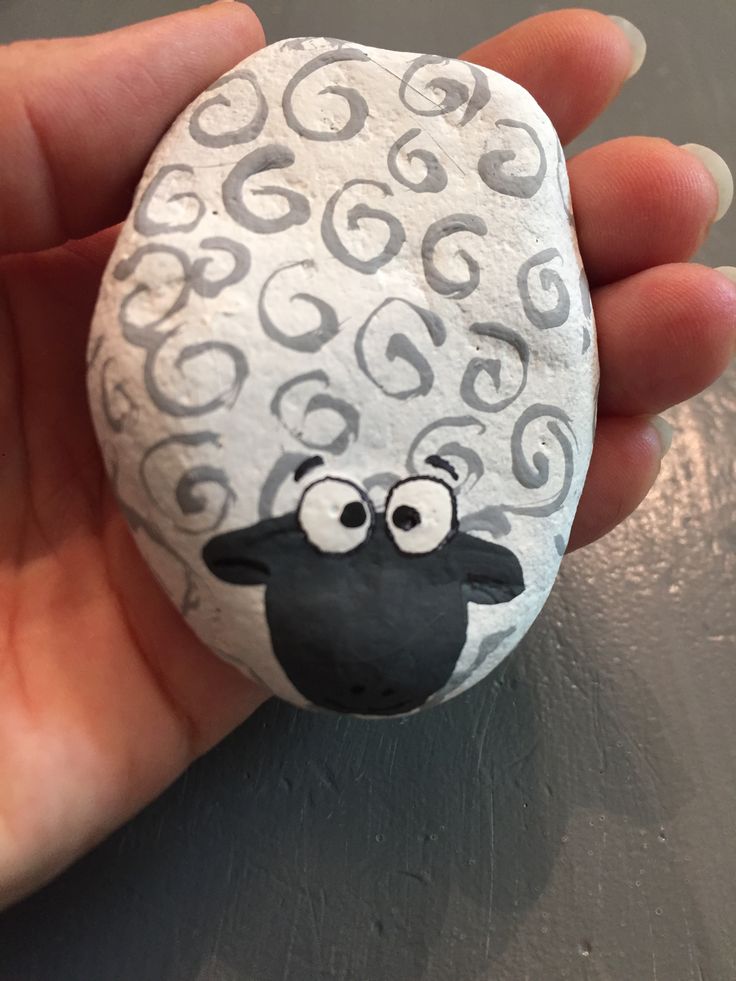 a hand holding a painted rock with a sheep on it's face and eyes