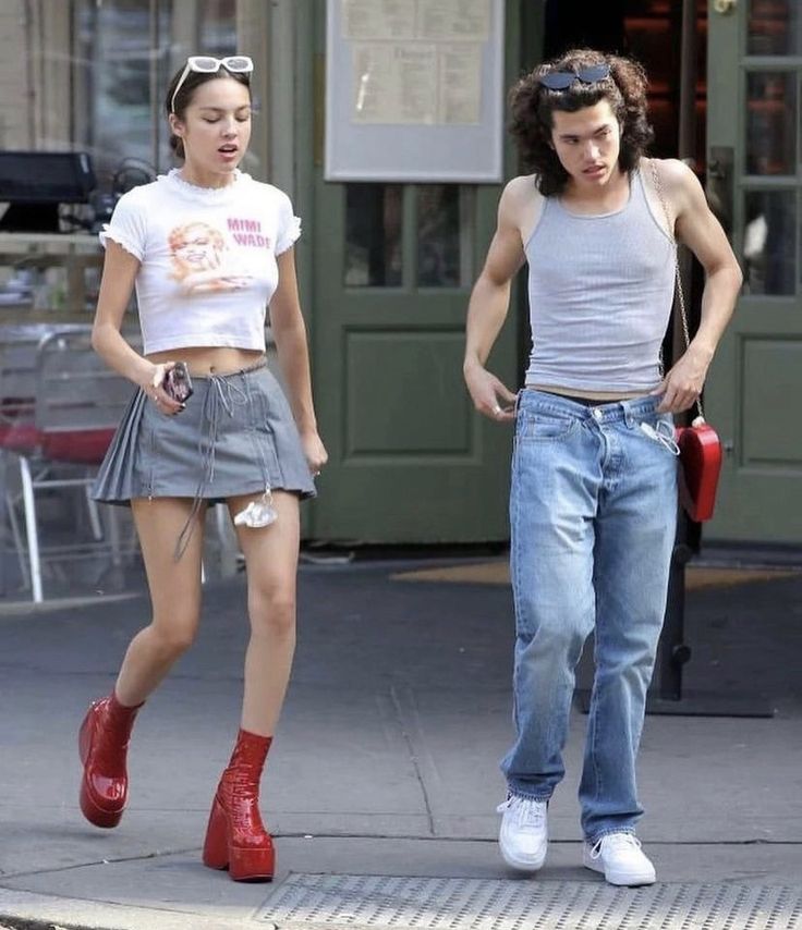 two people walking down the street with one person wearing red boots and another in white shirt