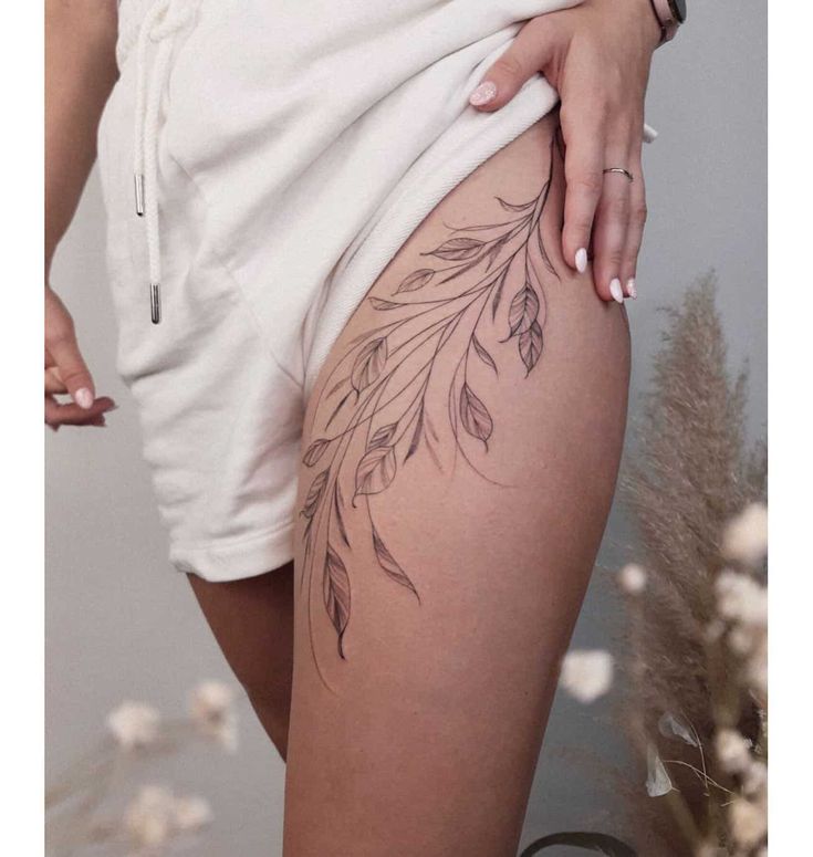 a woman with tattoos on her thigh wearing white shorts and holding a flower in her right hand