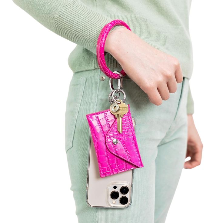 a woman holding a pink cell phone case with a keychain attached to it