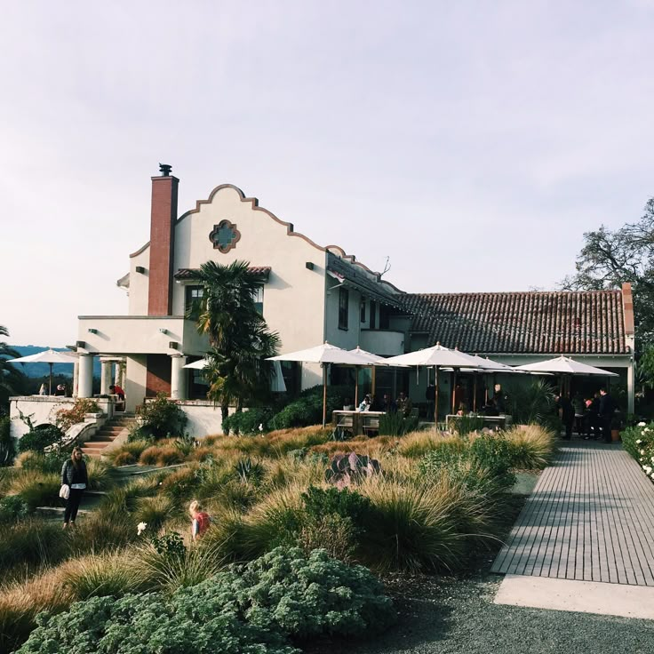 an outside view of a large house with lots of plants and people walking around it