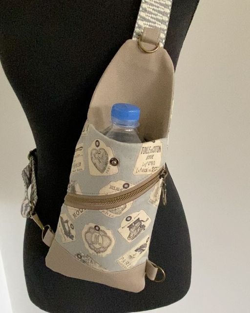 a woman's torso wearing a gray and white bag with blue water bottle in it