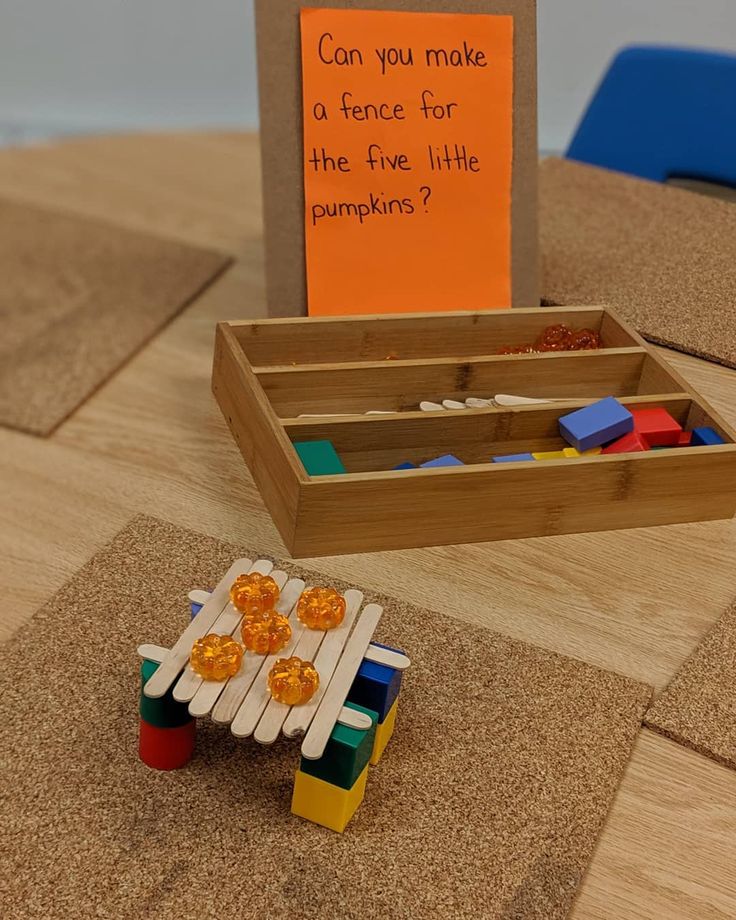 a wooden table topped with toys and a sign that says can you make a fence for the five little pumpkins?