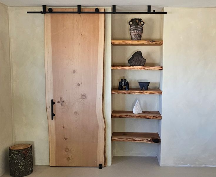 an empty room with shelves and vases on the wall next to a wooden door