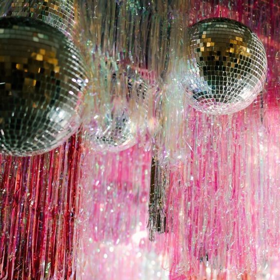 several disco balls hanging from the ceiling in front of pink curtained walls with streamers