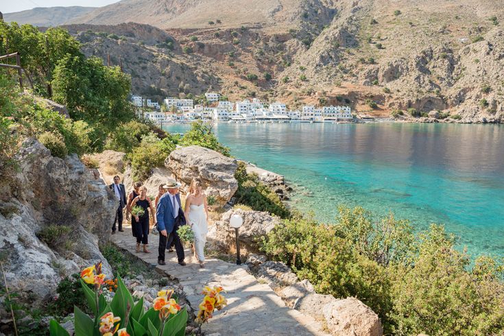 a group of people that are walking down some steps near the water with flowers in front of them