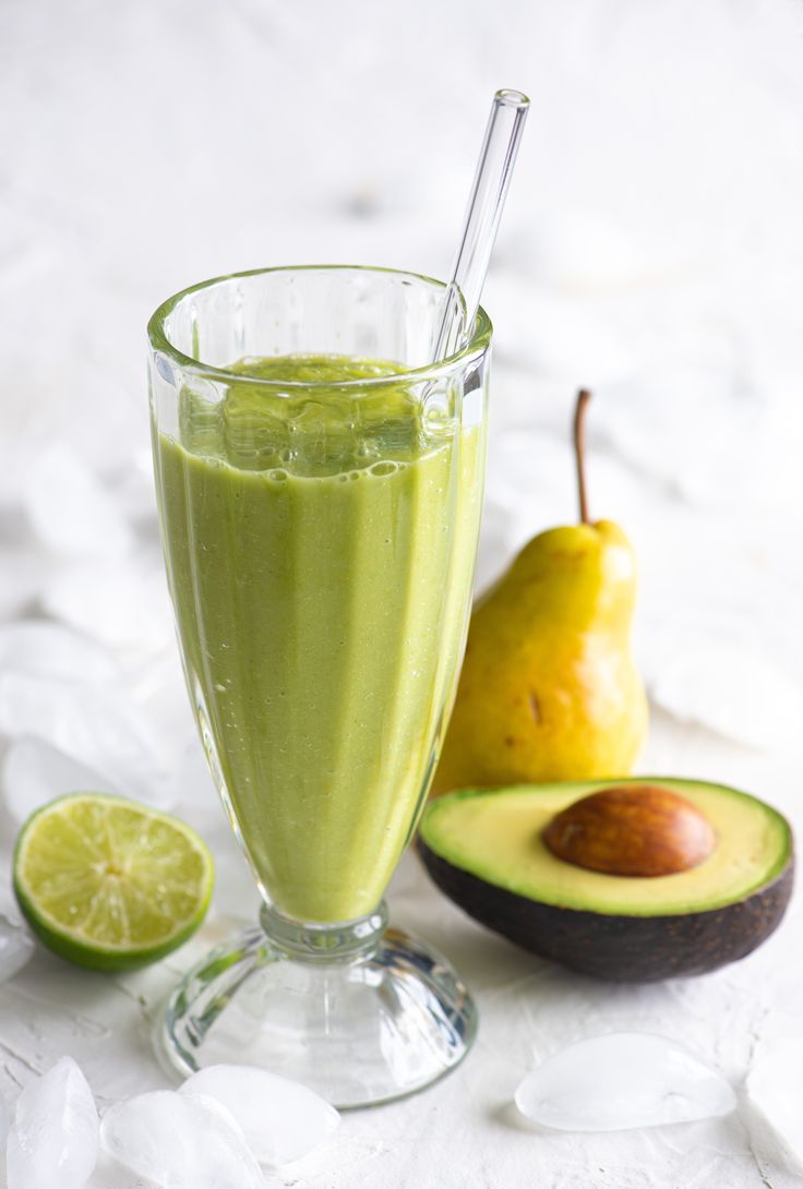 an avocado smoothie in a glass with a straw and two pieces of fruit next to it