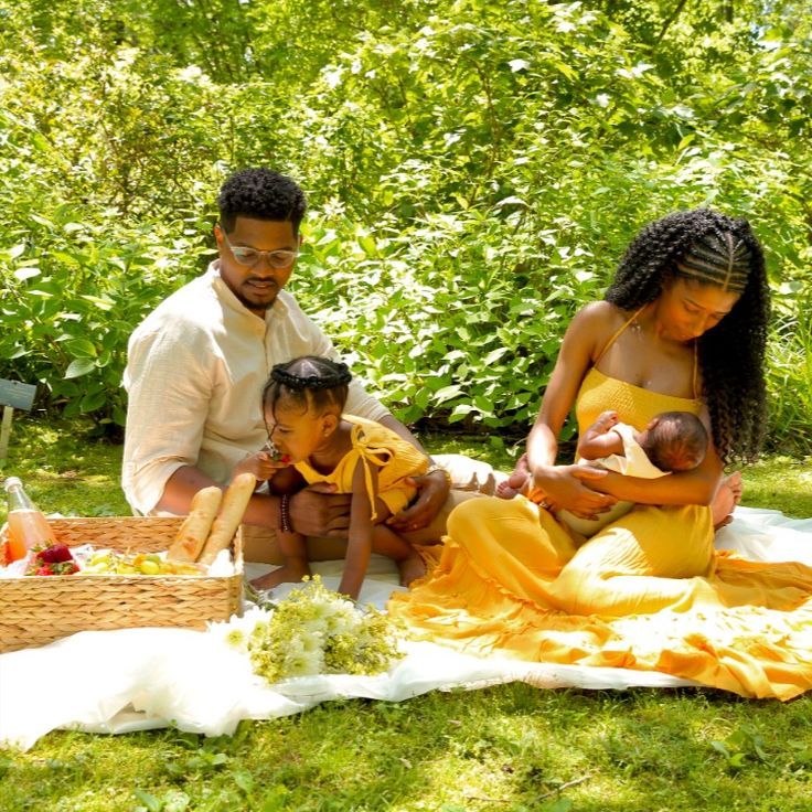 a man and woman with two children on a blanket in the grass near some trees