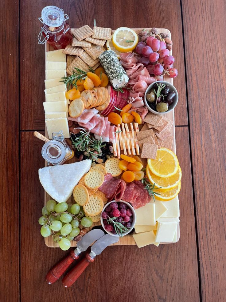 an assortment of cheeses, meats and fruit on a platter with crackers