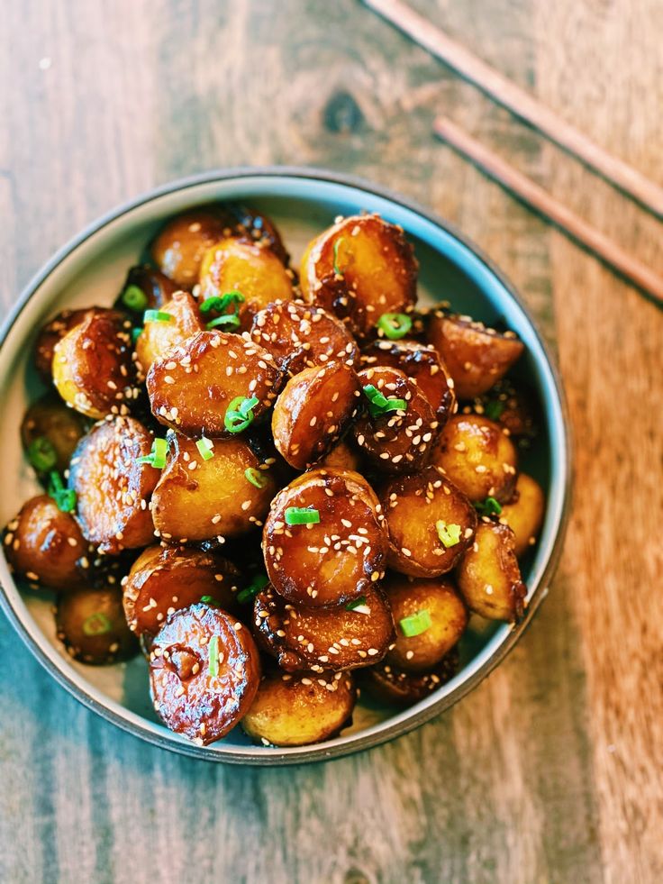 a bowl filled with fried food and chopsticks on top of a wooden table