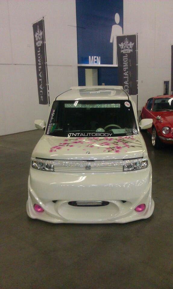 two cars parked in a showroom with pink flowers on the front and side windows